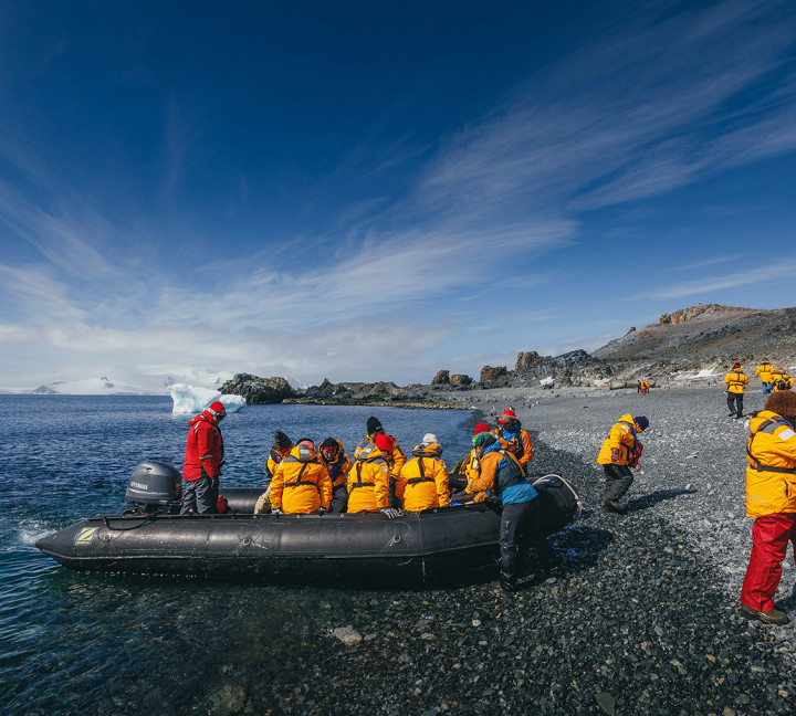 Expedition Guides help guests get out of their zodiac boats on a rocky beach at Half Moon Island.