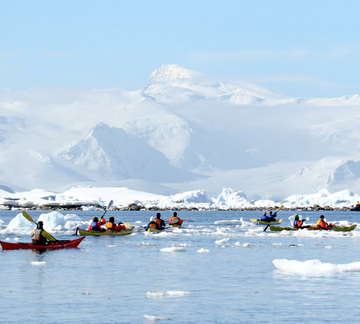 Guests kayaking through frigid waters in Antarctica. Two guides accompany the main group.