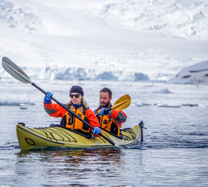 Two guests in their dry gear paddle a kayak in the frigid Antarctic waters during a sunny day.