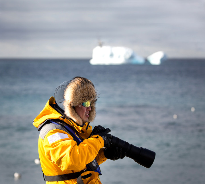 A guest in a yellow parka uses their telephoto lens during a landing in the Antarctic Peninsula.