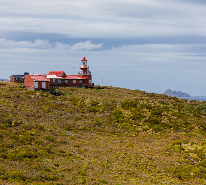 A red lighthouse sits on top of a grassy hill at Cape Horn.