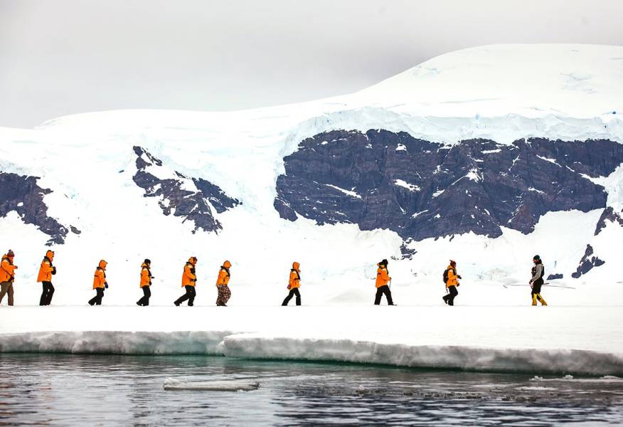 Guests in yellow parkas walk in a single file during a sea ice landing